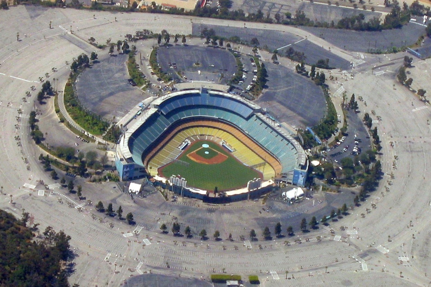A baseball stadium within a sea of asphalt and parking much larger than the stadium itself, with some trees here and there, small strips of green space, and no train stations, houses, etc. nearby