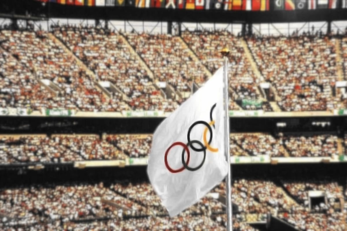 Crowd in an outdoor stadium in the day for the 1996 Atlanta Olympics with the Olympic flag in the middle of the frame